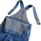 Close-up of a blue denim overall with adjustable shoulder straps and a front pocket, featuring a black-and-white gingham pattern lining and brass-tone snap buttons, on a white background.