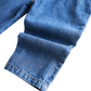 Close-up of blue denim fabric with a folded cuff showing tan contrast stitching on a white background.