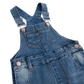 Close-up of a blue denim overall with adjustable shoulder straps, metal snap buttons, front patch pocket, and reinforced seams on a white background.