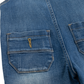 Close-up of blue denim jeans showing a front patch pocket with contrast stitching and a small yellow embroidered detail.